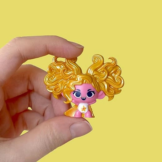 Small figurine with pink face and yellow hair held by a hand against a yellow background