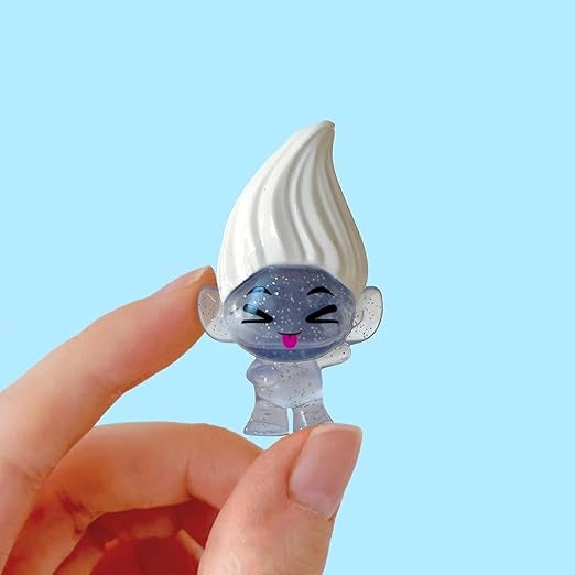 Small figurine of a character with a white hat and blue face held by a hand against a light blue background