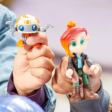 Two toy figures, one robot-like and one with red hair, held by a person against a blurred background.
