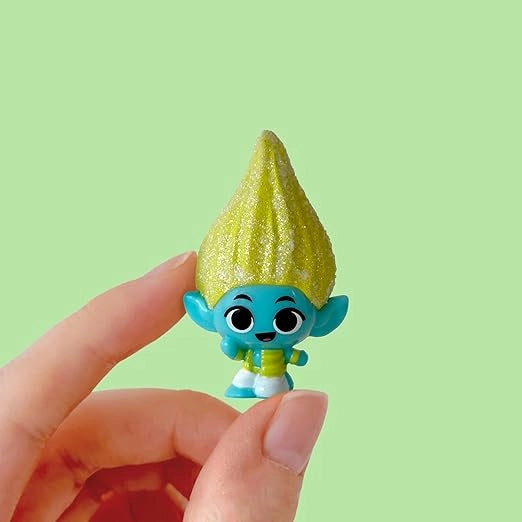 Small figurine with a yellow hat and blue body held by a hand against a green background
