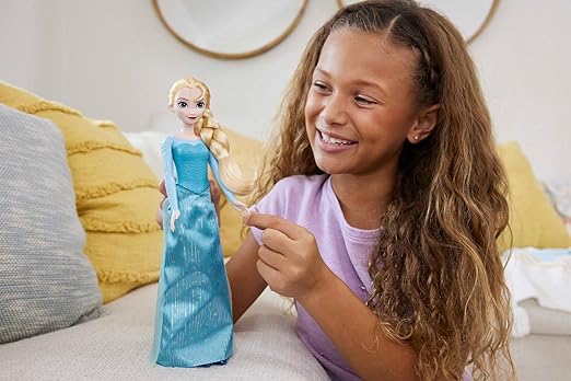 A girl is playing with Mattel Disney Frozen Elsa Doll in signature blue dress with removable cape and skirt. Posable for creative play. Inspired by Frozen movies.