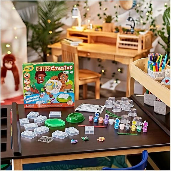 Crayola Critter Creator Fossil Kit on a table with various craft supplies in a classroom setting.