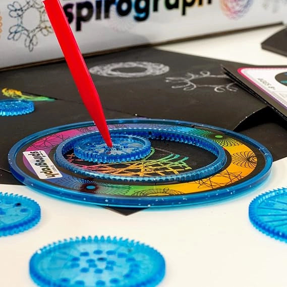 Spirograph toy set with a red pen and colorful plastic gears on a white surface.