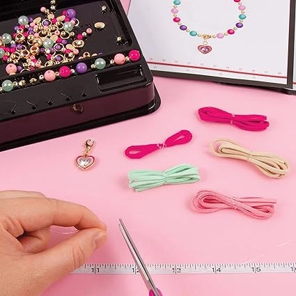 Jewelry-making kit with beads, charms, and ribbons on a pink surface.