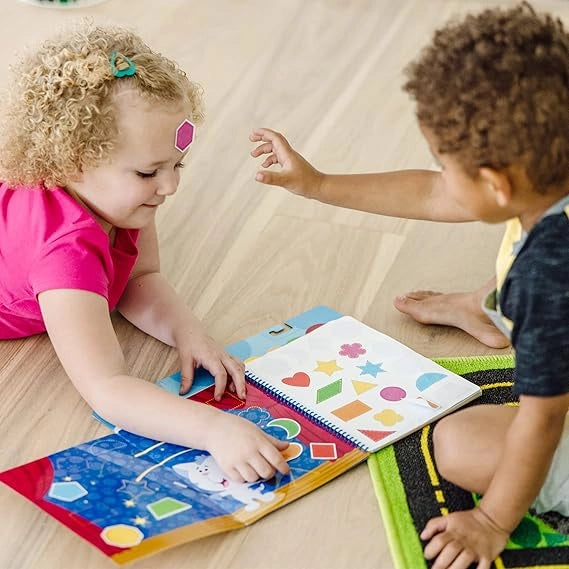 Two children interacting with a colorful book on a wooden floor.
